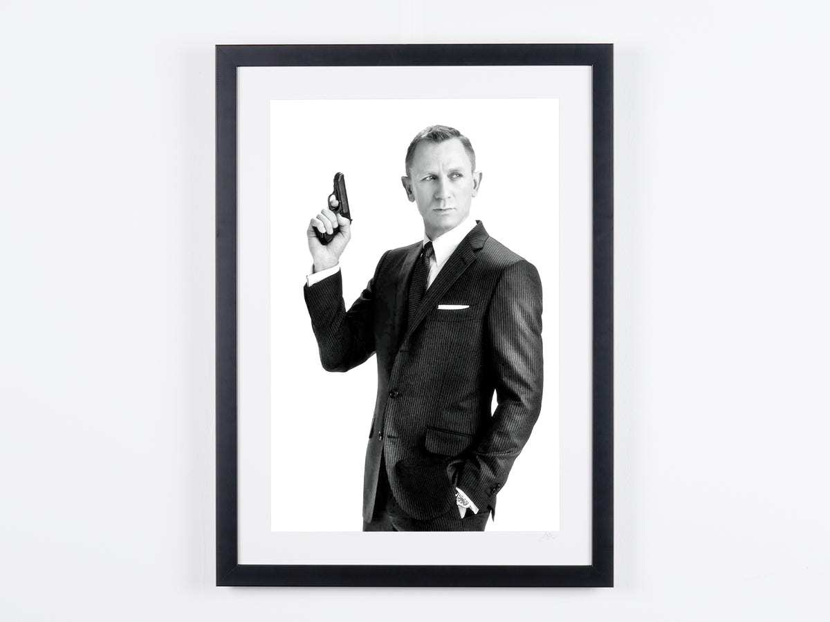 Photographie d’art de Daniel Craig dans Daniel Craig en costume, l’arme levée, encadrée à la main — édition limitée de 30 exemplaires numérotés.