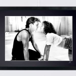Black-and-white landscape photograph of Patrick Swayze and Jennifer Grey face to face on the floor of an empty dance studio.