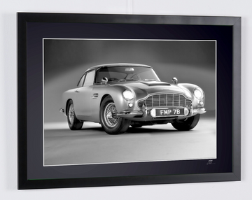 James Bond 007 : Goldfinger (1964) — Aston Martin DB5, coche de tres cuartos delantero sobre fondo liso, con matrícula FMP 7B visible, fotografía de cine enmarcada en blanco y negro, marco visto en perspectiva desde la derecha.