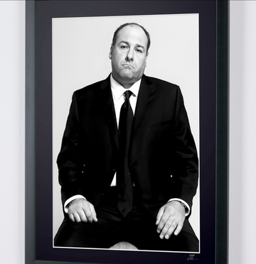 James Gandolfini en Los Soprano — Serie de TV (1999–2007), retrato sentado con traje oscuro y corbata y las manos sobre los muslos, fotografía de cine enmarcada en blanco y negro, otro detalle de la impresión y del paspartú.