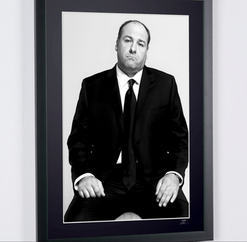 James Gandolfini en Los Soprano — Serie de TV (1999–2007), retrato sentado con traje oscuro y corbata y las manos sobre los muslos, fotografía de cine enmarcada en blanco y negro, detalle de la fotografía y del paspartú.