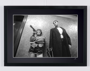 Graphic black-and-white photograph of Natalie Portman and Jean Reno standing motionless in a corridor with textured metal walls.