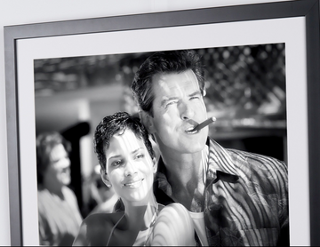 Pierce Brosnan en Halle Berry in James Bond 007 : Die Another Day (2002), naast elkaar glimlachend, Pierce Brosnan met een sigaar in zijn mond, ingelijste filmfoto in zwart-wit, detail van de bovenkant van de foto en lijst.