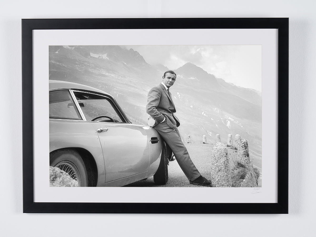 James Bond 007: Goldfinger (1964) - Sean Connery leunend op de Aston Martin DB5, bergdecor — ingelijste filmfoto