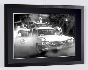Ghostbusters (1984) — Ecto-1, Ecto-1 car seen from the front, with a door open and smoke near the ground, framed cinema photograph in black and white, frame viewed in perspective from the right.