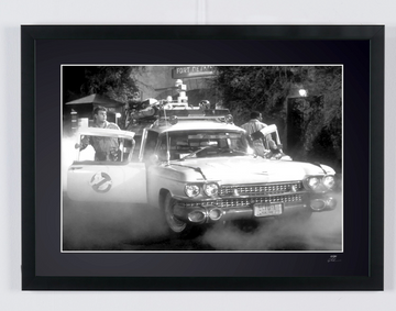 Ghostbusters (1984) — Ecto-1, Ecto-1 car seen from the front, with a door open and smoke near the ground, framed cinema photograph in black and white, front view of the frame.